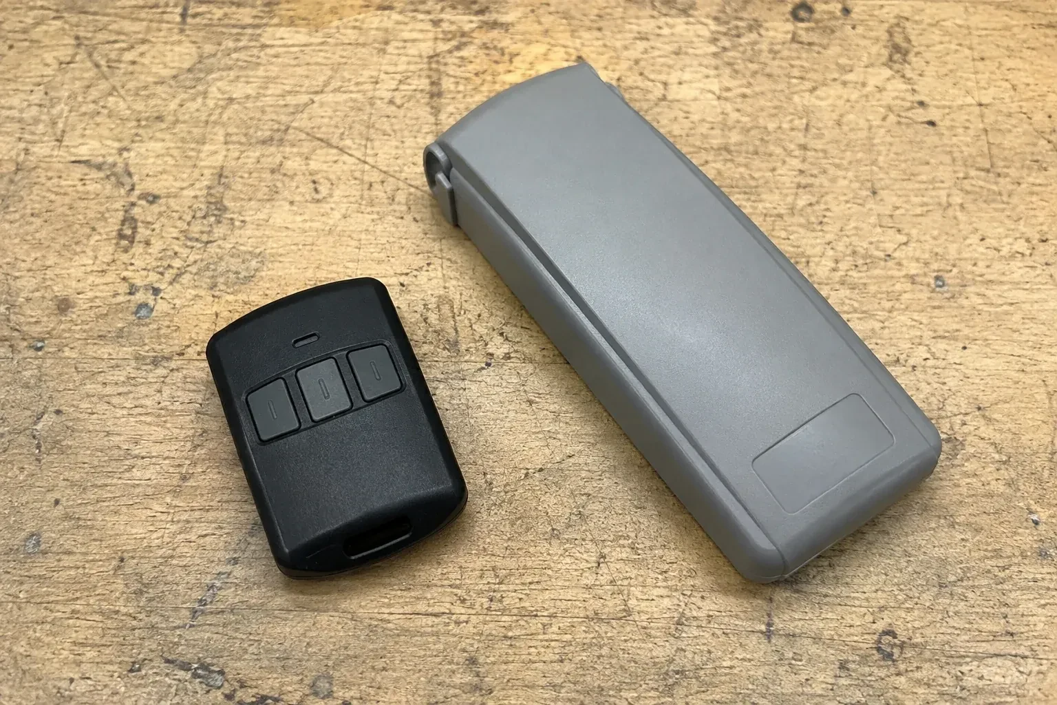 Three-button remote beside a closed grey keypad cover on a workbench. — Garage Door Remote and Keypad Programming, Toronto