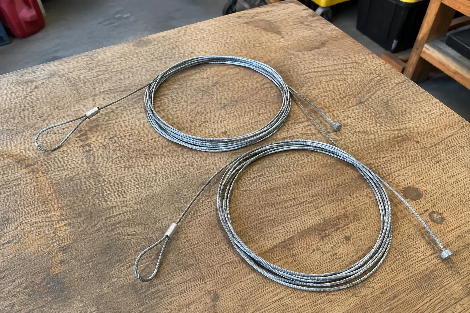 Two coiled steel cables with loop and stop ends on a workbench. — Garage Door Cable Replacement, Toronto